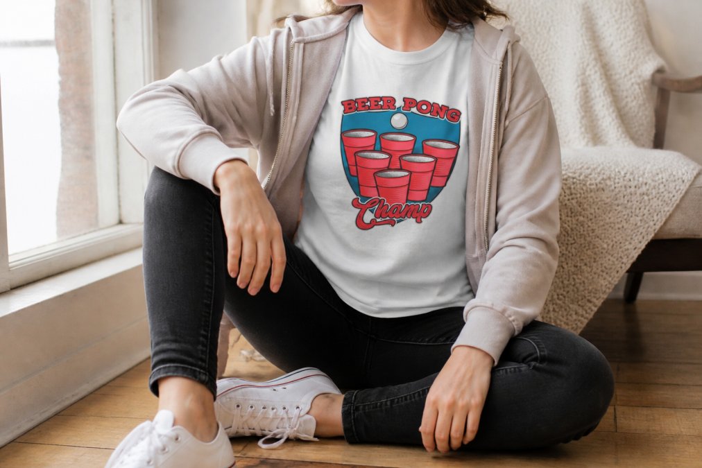 Close-up of someone styling a graphic tee with fitted dark jeans and white sneakers, showing casual college-appropriate outfit layering with natural window lighting