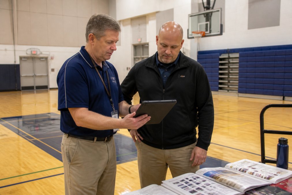 School staff reviewing a budget and catalog for affordable gym equipment in a high school gymnasium
