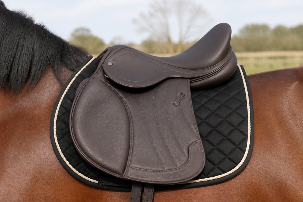 Close-up of a properly fitted saddle positioned on a horse's back with a groomed saddle pad underneath, showing correct alignment with the horse's spine and even panel contact, natural outdoor lighting