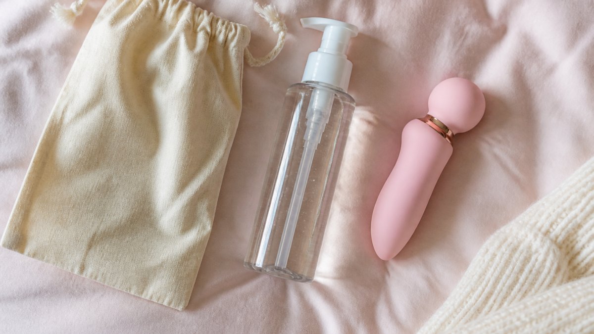 A neat flat lay of affordable intimate wellness essentials on a soft pastel background, including a water-based lubricant bottle, a small silicone massager, and a cotton pouch