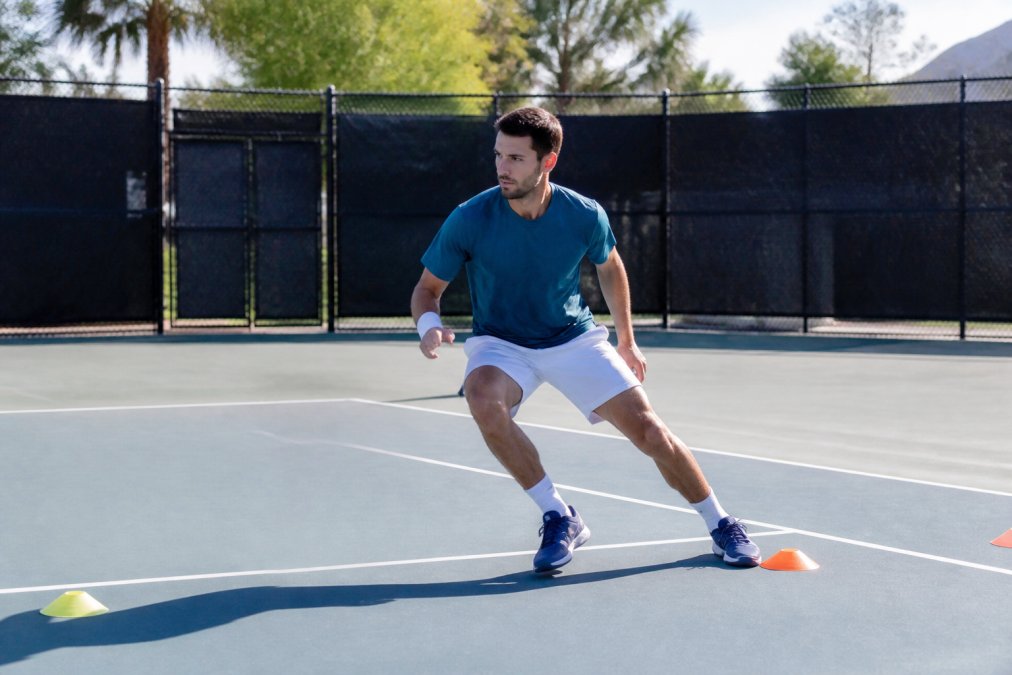 Tennis player practicing footwork drills alone on a public court, executing quick lateral movements with focused intensity and proper posture