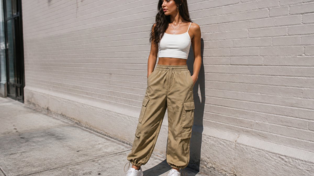 Woman in high-waisted khaki cargo pants and a crop top standing against a brick wall in a city setting