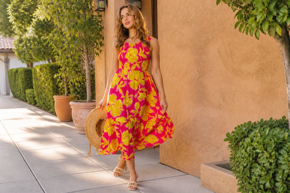 A woman in a flowy floral midi dress standing outdoors on a sunny day, accessorized with strappy sandals and a straw bag, golden afternoon light, relaxed and confident posture