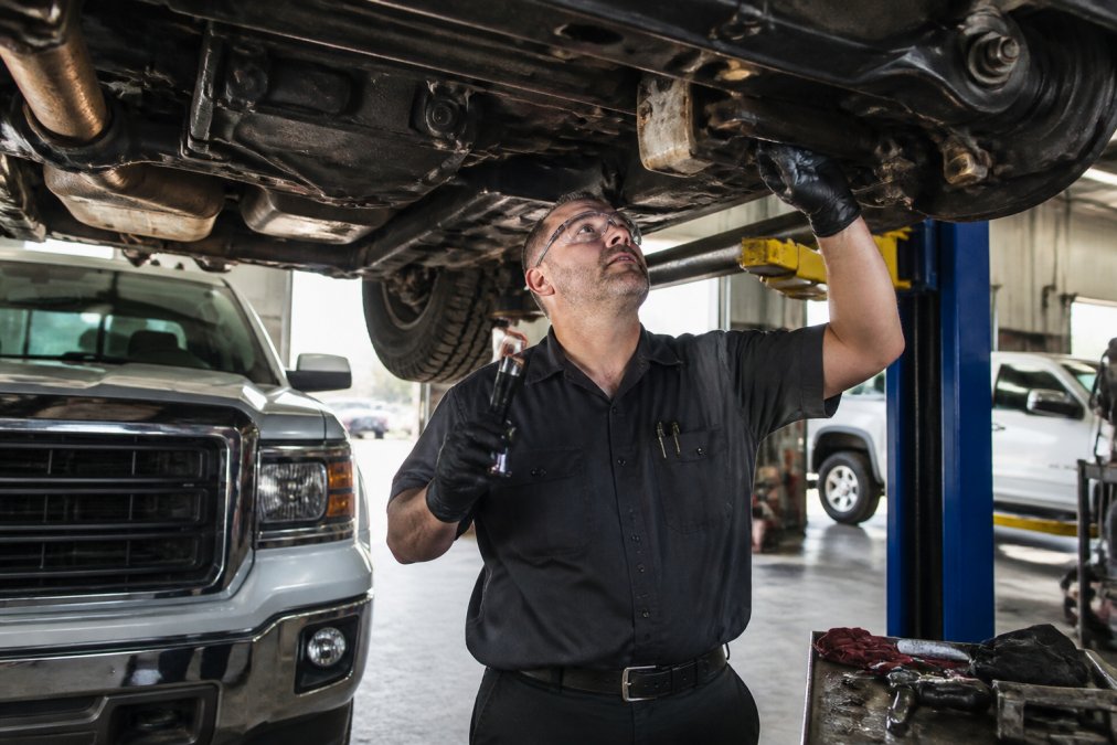 Technician inspecting a used truck with low mileage in a service bay during a professional bumper-to-bumper check.