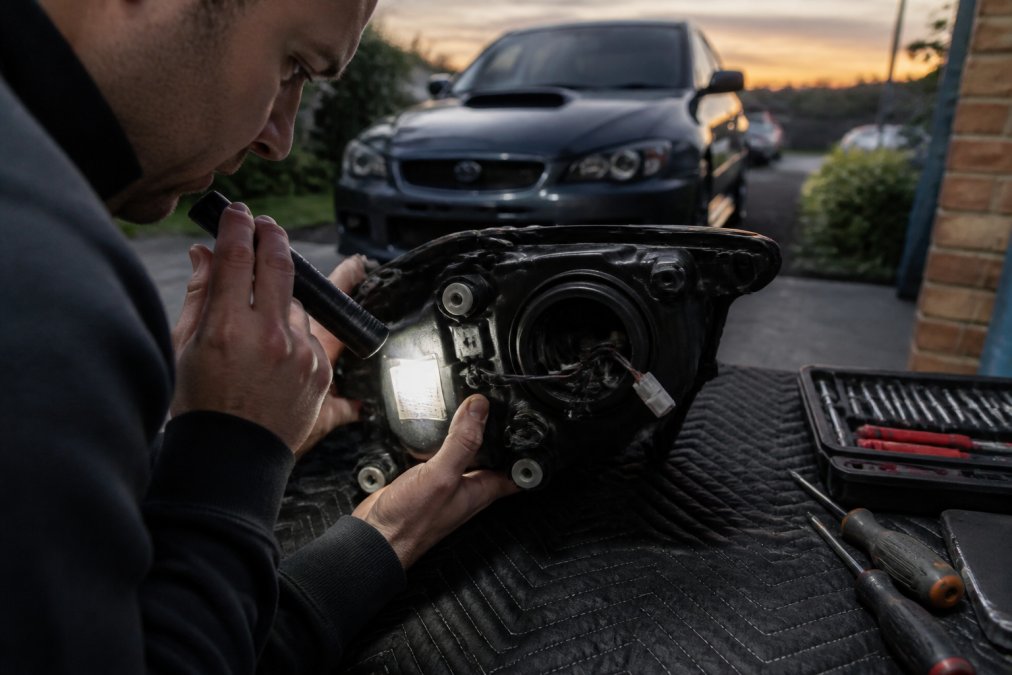 Person using a flashlight to inspect a compliance label on projector headlights legal for road use at dusk.