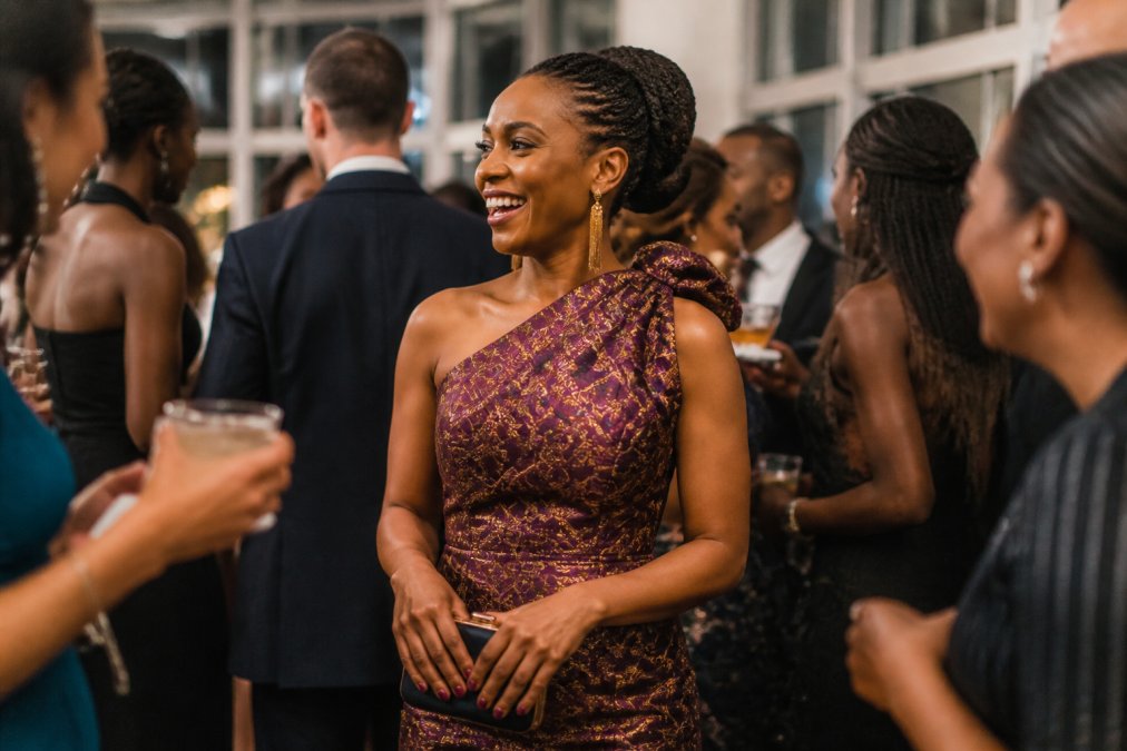 Woman wearing an elegant KAHINDO dress in rich jewel tones at a formal evening event, showcasing the artisan craftsmanship and vibrant African-inspired print details and metallic threading