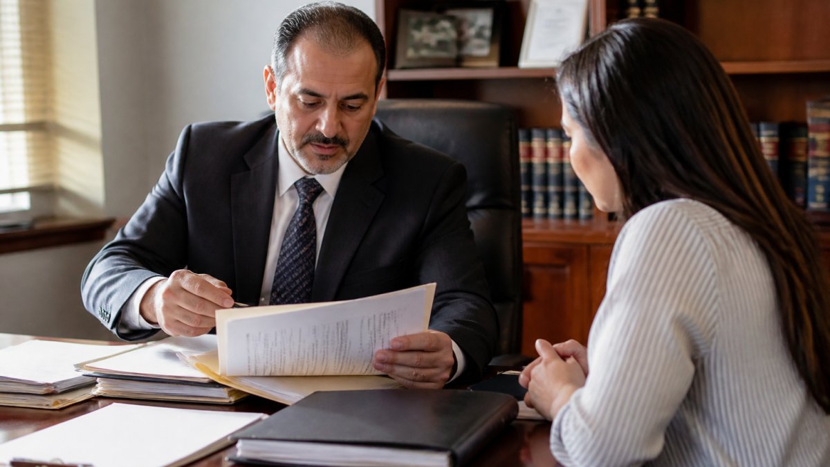 Professional immigration attorney meeting with client in Arizona law office, reviewing case files and discussing conviction records on desk with natural office lighting