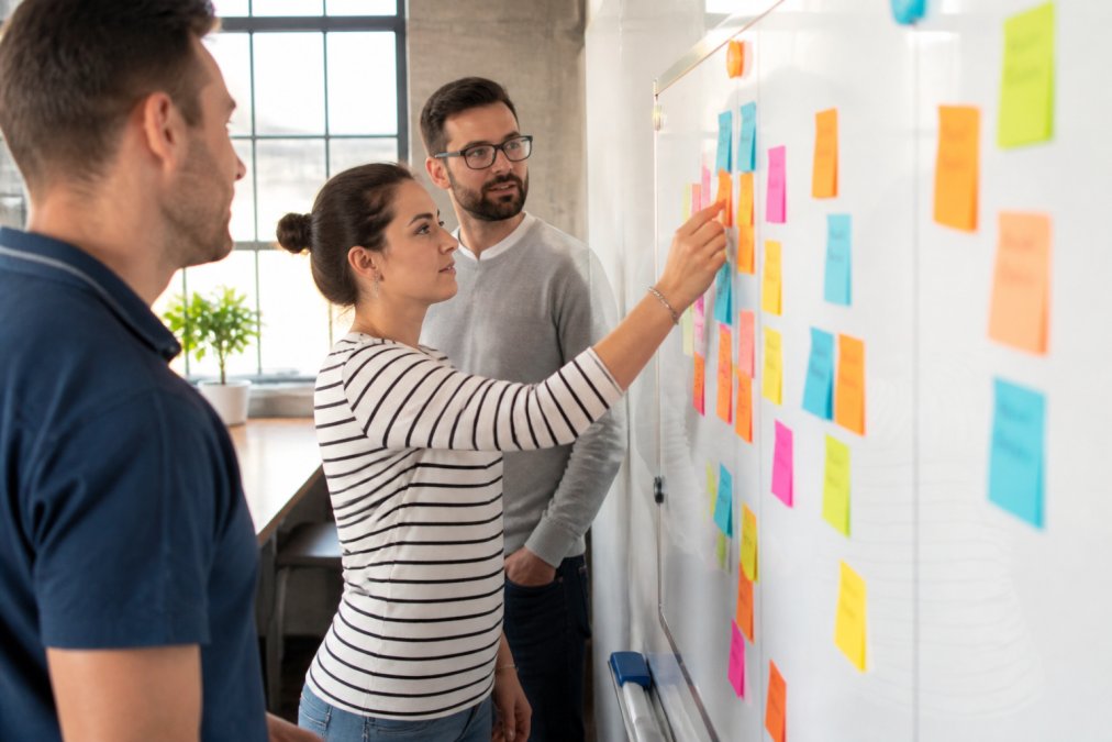 A small team of software developers collaborating around a whiteboard covered with sticky notes and sprint tasks in a bright modern office, natural daylight streaming through windows