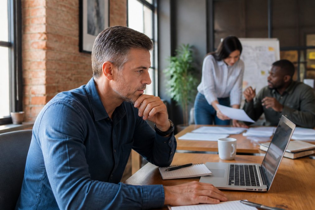 Small business owner reviewing AI workflow automation on a computer screen in their office, with team members collaborating in background