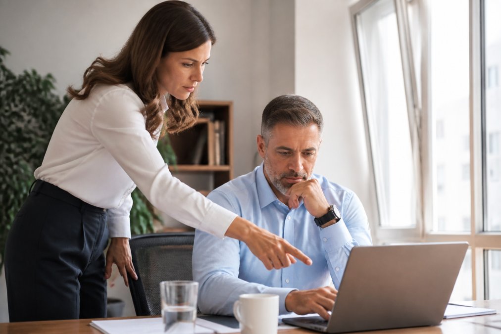 A sales manager reviewing a laptop dashboard with pipeline metrics while a colleague points at the screen in a bright modern office