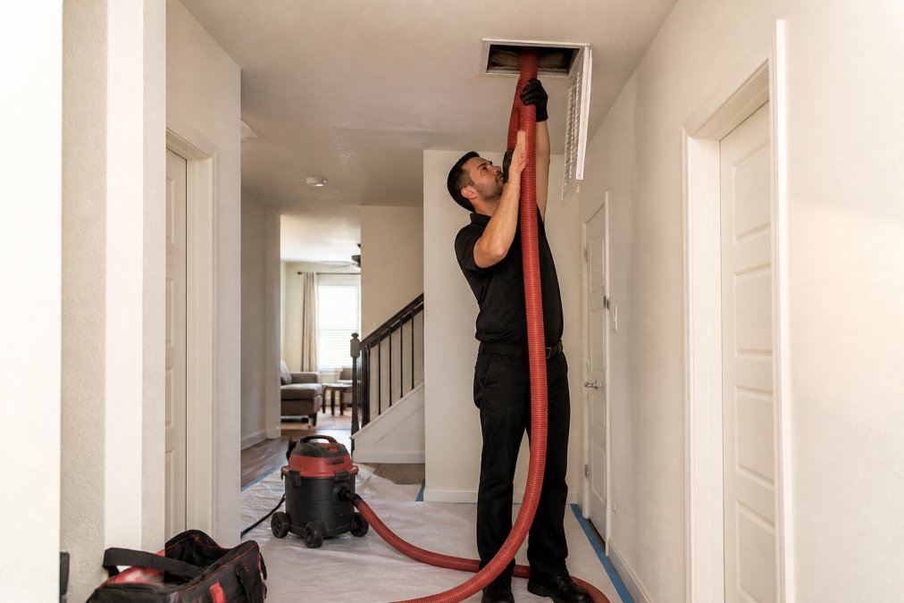 Technician using a vacuum hose during an air duct cleaning service in a home
