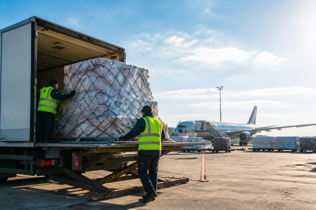 Cargo handlers coordinating freight between a truck and plane for an air freight forwarder at an airport.