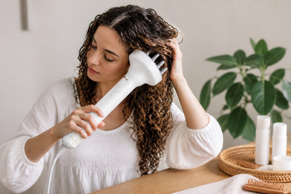 Woman using an air styling tool with a diffuser attachment on damp curly hair, demonstrating proper tool positioning and technique with natural studio lighting