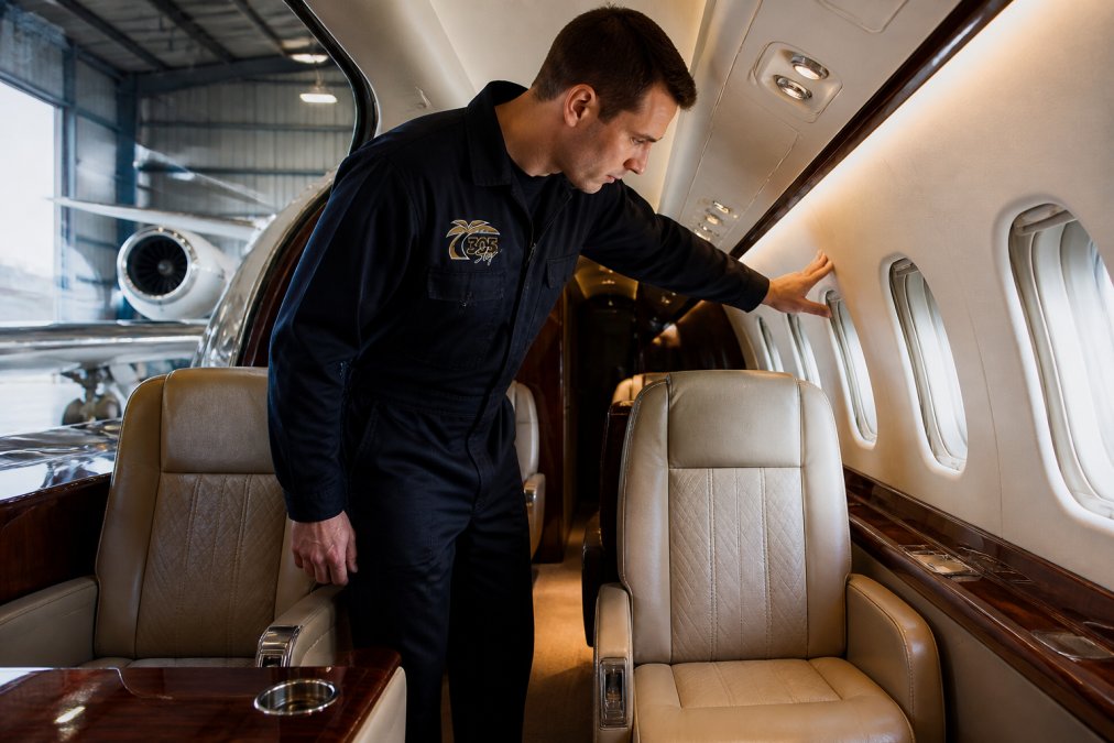Technician inspecting leather seats and wood panels after a cabin interior transformation in a bright hangar