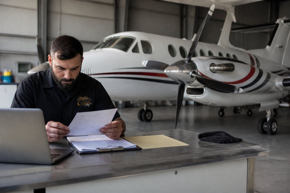 A&P mechanic reviewing aircraft maintenance liability insurance documents near a King Air in a hangar