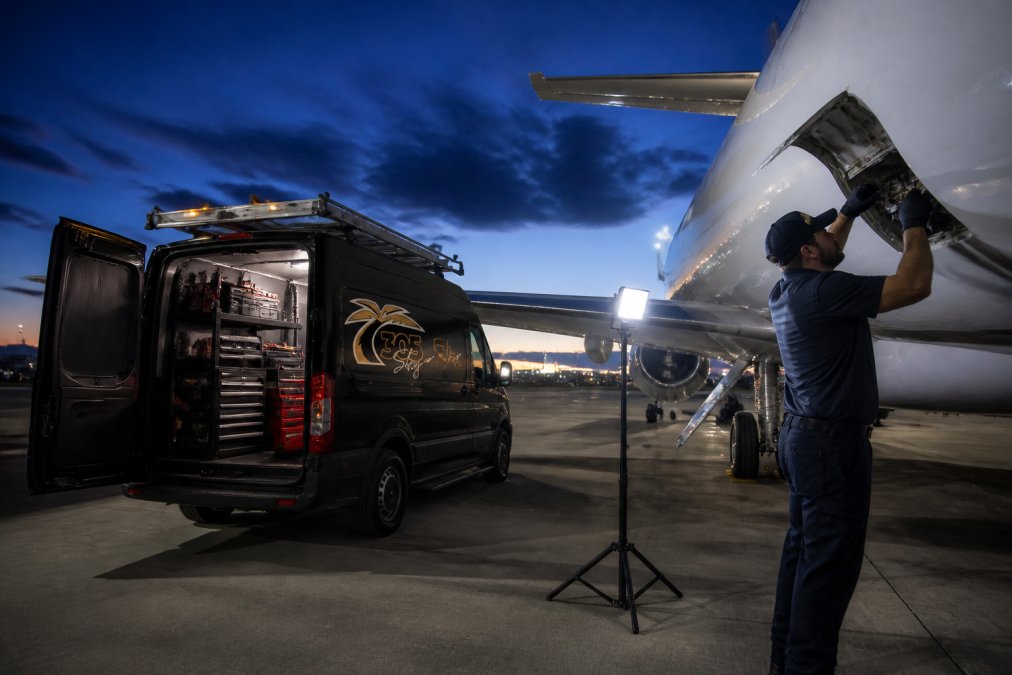Mobile maintenance van parked beside aircraft on tarmac during evening emergency repair, technician in uniform working on aircraft exterior with diagnostic equipment visible