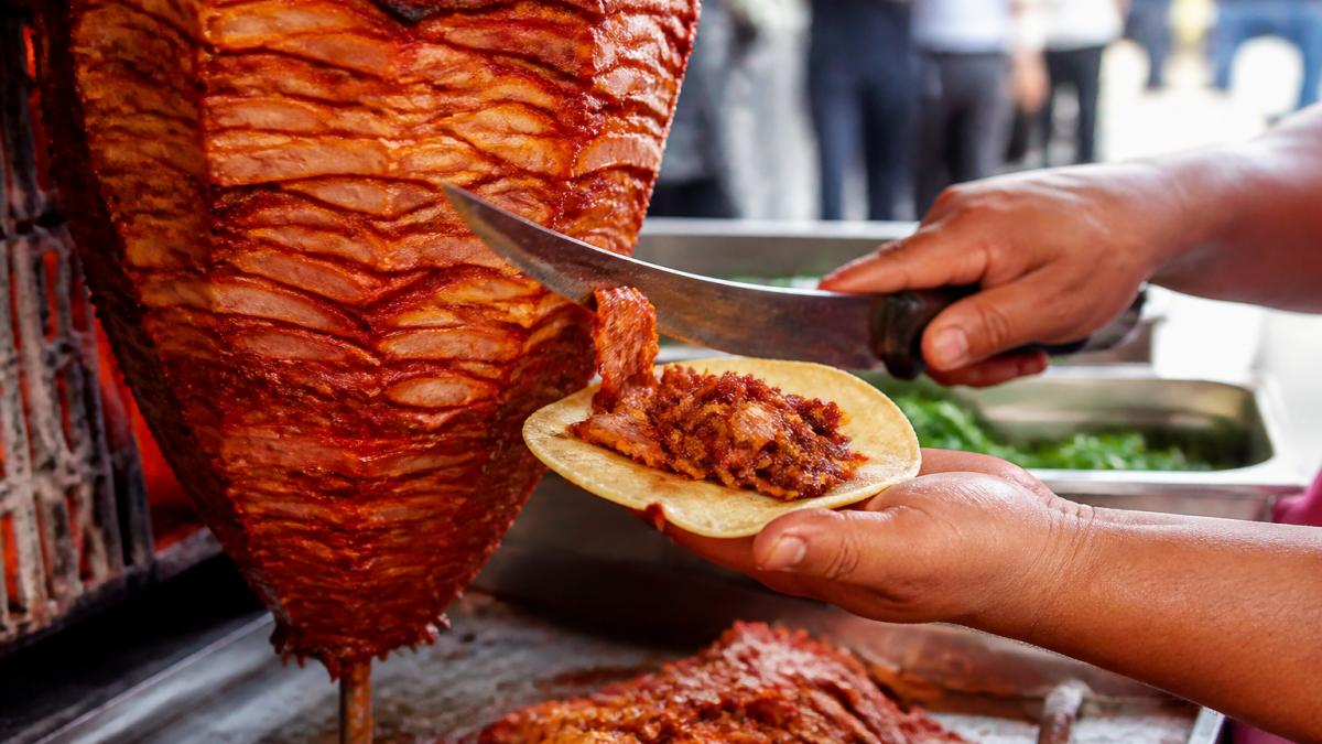 Thinly sliced al pastor pork carved from a vertical trompo onto a warm corn tortilla for a comparison of al pastor vs carne