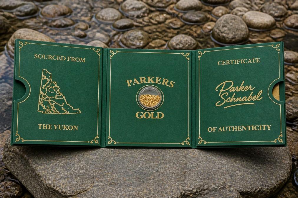 Raw placer gold flakes displayed in an open tri-fold presentation case with Certificate of Authenticity visible on cream-colored card stock, natural lighting highlighting the gold's natural texture