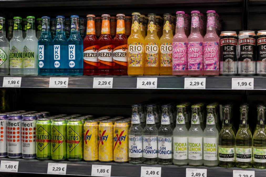 Bunte Alkopops in Flaschen und Dosen im Regal als Basis für die Alkopops Definition Steuer Diskussion.