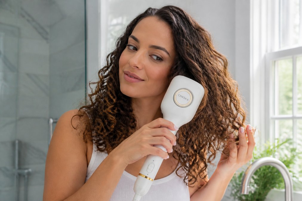 Woman with thick, curly hair styling her hair with a multi-tool styler, showing the versatility of attachments and ease of use in a modern bathroom setting with natural window lighting