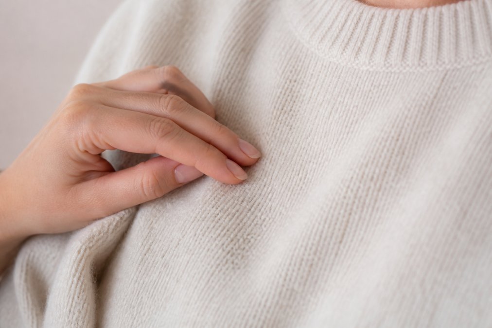 Close-up of a person's hand gently touching a soft, cream-colored alpaca sweater, showing the fine texture against their skin in soft natural lighting