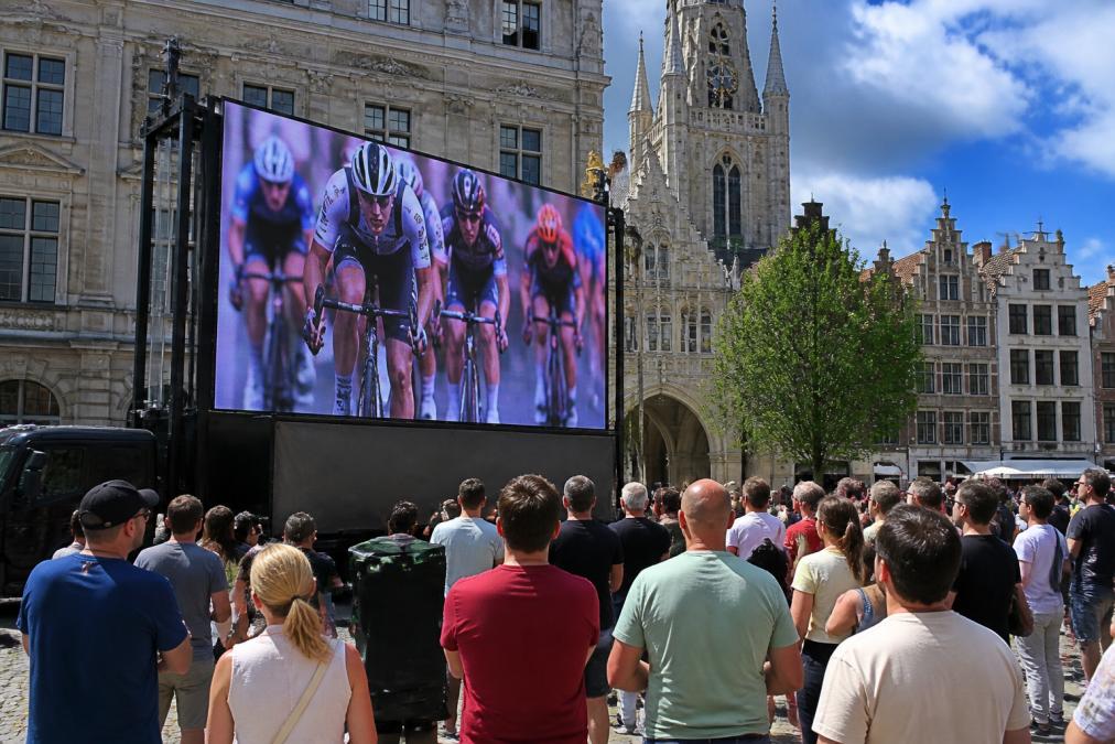Een groot mobiel LED-scherm op een aanhangwagen tijdens een buitenevenement in een stadscentrum, met publiek dat in helder daglicht naar het scherm kijkt