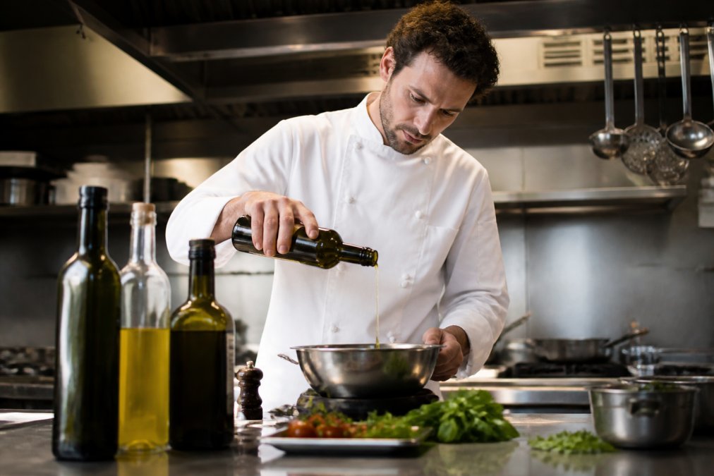 Professionele keuken met flessen premium olijfolie op de werkbank, waarbij een chef in wit uniform de olie voorbereidt voor gebruik in een modern restaurant