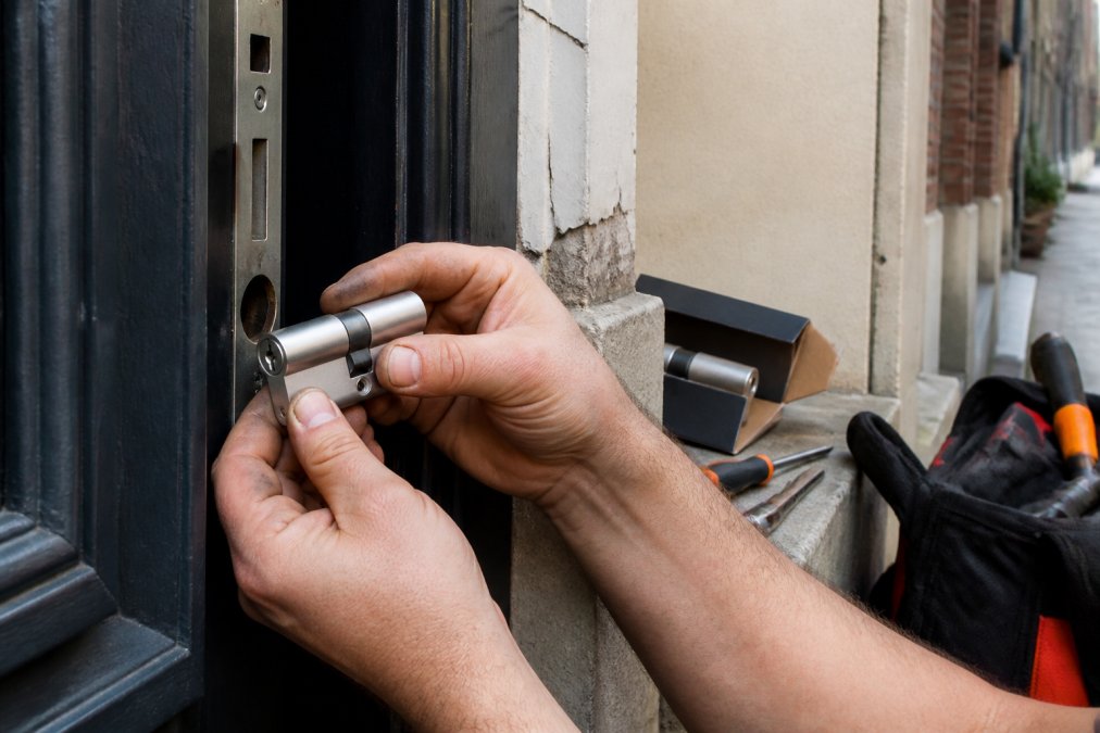 Close-up van ervaren handen die een veiligheidscilinder met kerntrekbeveiliging in een voordeur plaatsen, met gereedschap en een cilinderdoos op de achtergrond in een Antwerps rijhuis
