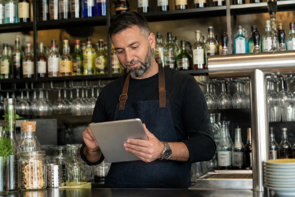 Dueño de un bar revisando el panel de gestión en una tablet detrás de la barra de un local moderno