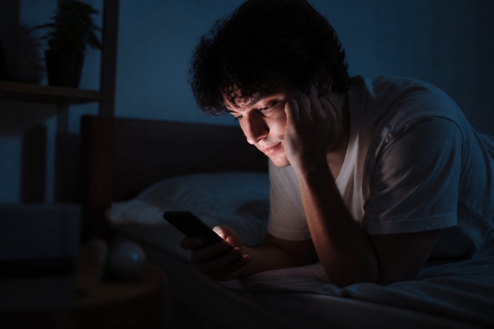 Persona che guarda il telefono di notte in un ambiente tranquillo e sicuro, con la luce dello schermo che illumina il viso, rappresentando l'accesso al supporto emotivo in qualsiasi momento