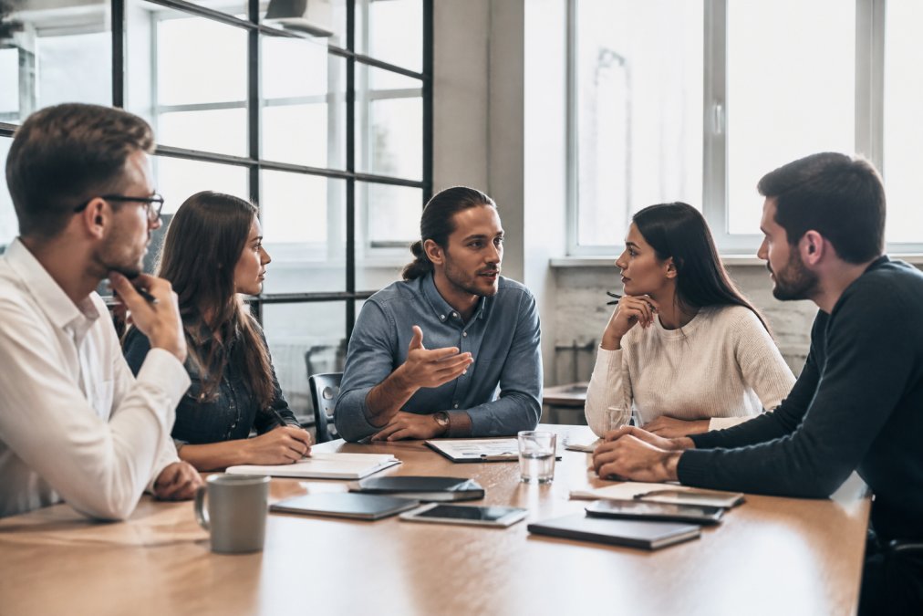 Team von Unternehmern in einem modernen Büro bei einer Besprechung, diskutiert Geschäftsstrategie an einem Konferenztisch mit Laptop und Notizbüchern