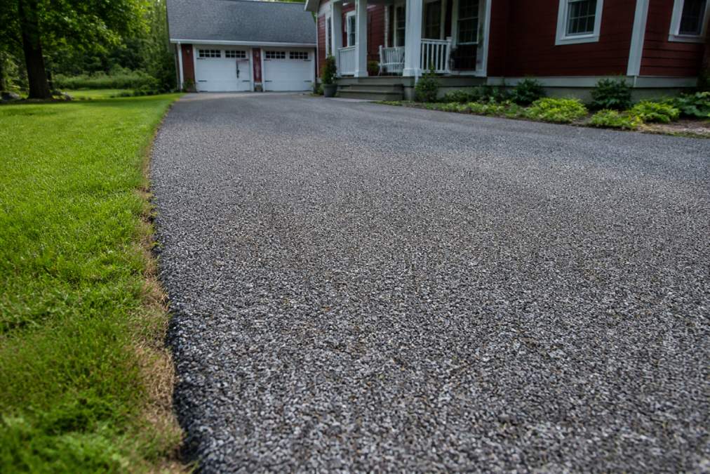 A residential driveway with a fresh tar and chip surface, showing the textured stone finish and a clear edge along the grass