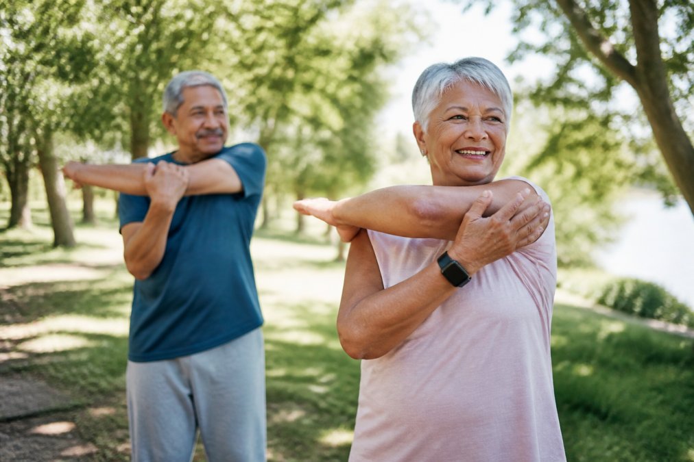 Active older adult practicing gentle stretching and movement outdoors in natural sunlight, demonstrating low-impact exercise for joint mobility and flexibility