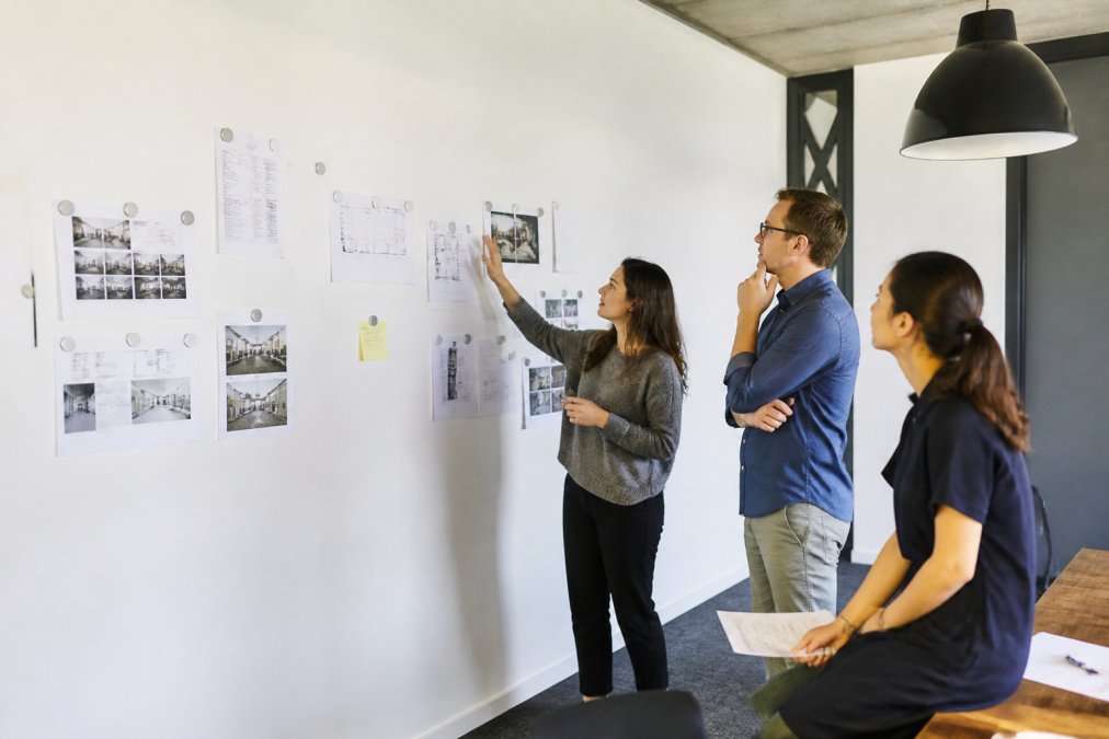 Modern office meeting room with a full white magnetic wall displaying project timelines and documents held with steel magnets, team members collaborating around the space