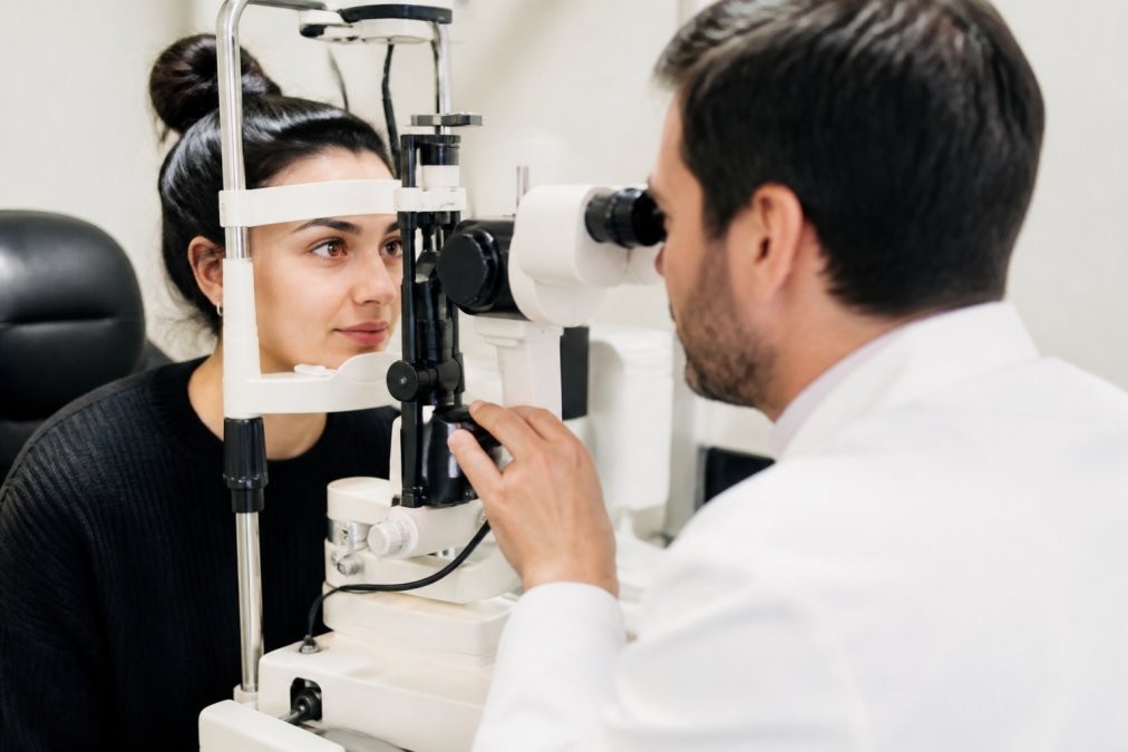 Professional eye care provider examining patient's eye using advanced diagnostic equipment in modern ophthalmology clinic with clinical lighting