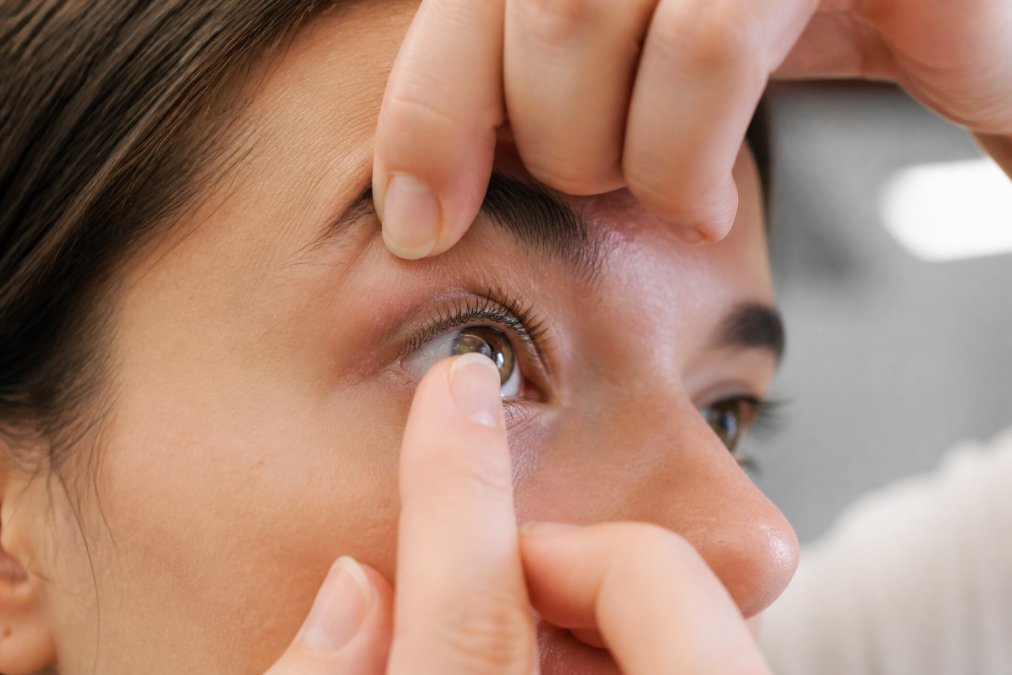 Close-up of person's hands carefully inserting contact lens into eye, showing precision and steady technique in well-lit setting