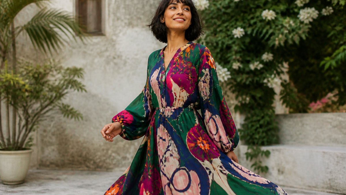 Person wearing a vibrant, statement-printed dress with bold artistic designs in jewel tones, styled confidently outdoors in natural daylight, showcasing personal expression through fashion