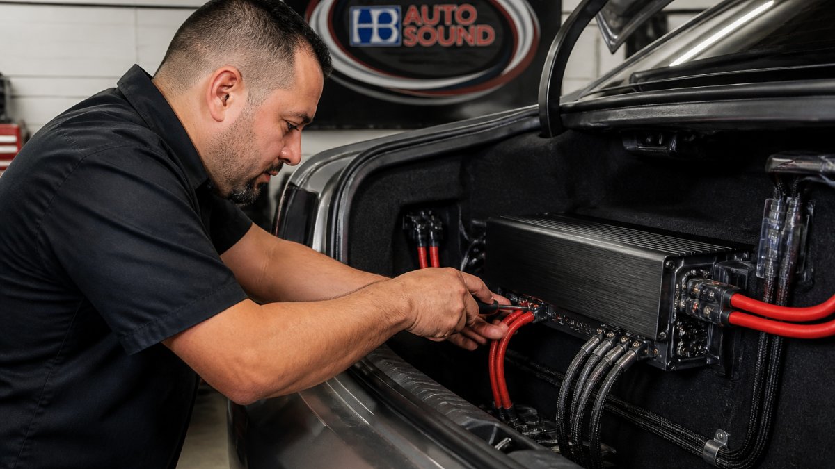 Professional demonstrating car amplifier installation with power cables and wiring connections in vehicle trunk with proper cable management