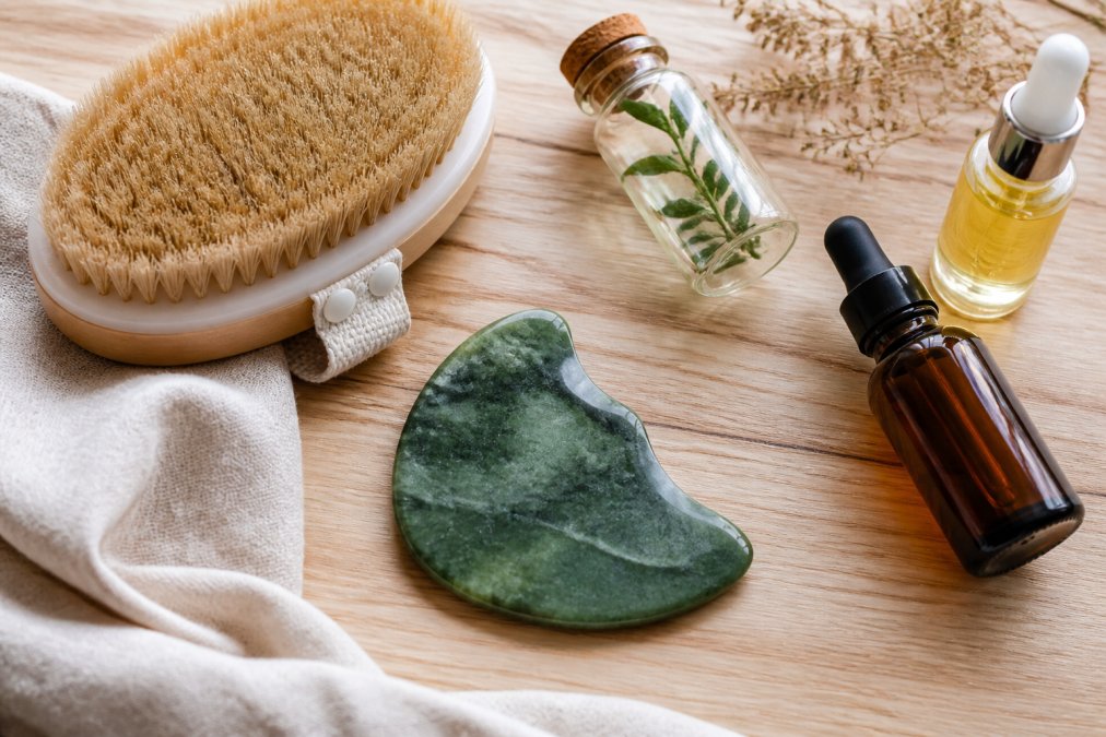 Dry brush, gua sha stone, and essential oils arranged on wood as lymphatic drainage alternatives for home use.