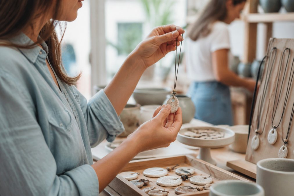Woman examining a detailed ceramic charm necklace featuring handcrafted goods at a bright boutique counter