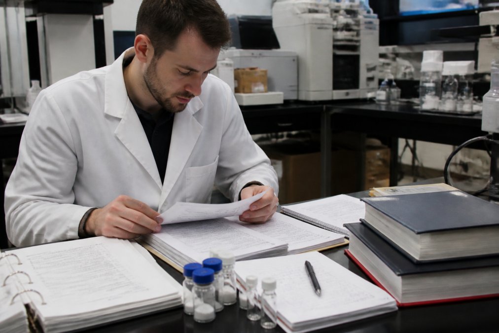 Researcher carefully reviewing laboratory documentation and research protocols at a desk surrounded by peptide reference materials, analytical equipment specifications, and study design notes in a professional research environment