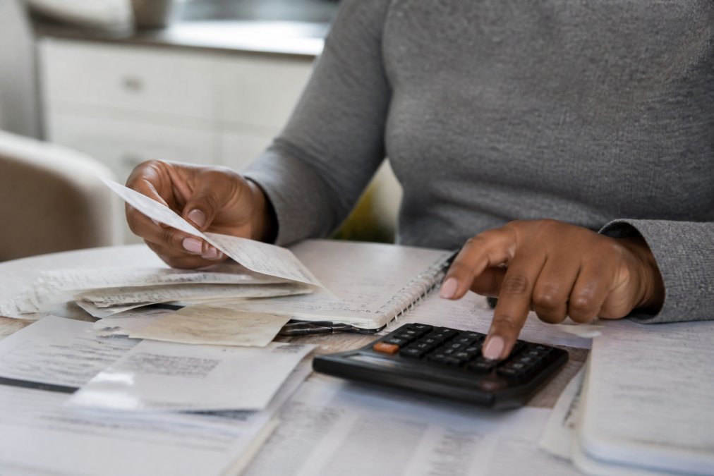 Close-up of hands organizing bills, receipts, and documents on table with calculator and notebook for tracking expenses
