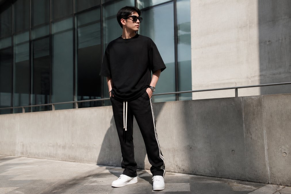 Young adult in an oversized t-shirt and track pants standing in a bright urban setting for a relaxed look