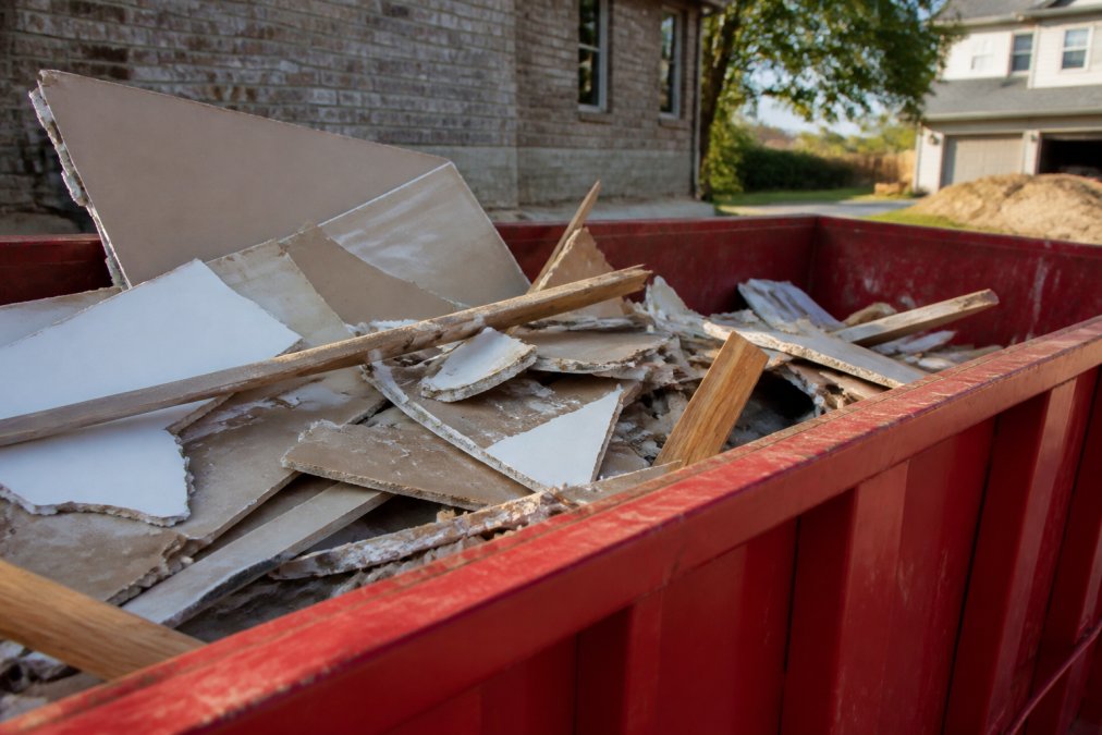 Close-up of construction debris including drywall pieces, wood scraps, and miscellaneous demolition materials being loaded into a residential roll-off dumpster on a sunny afternoon