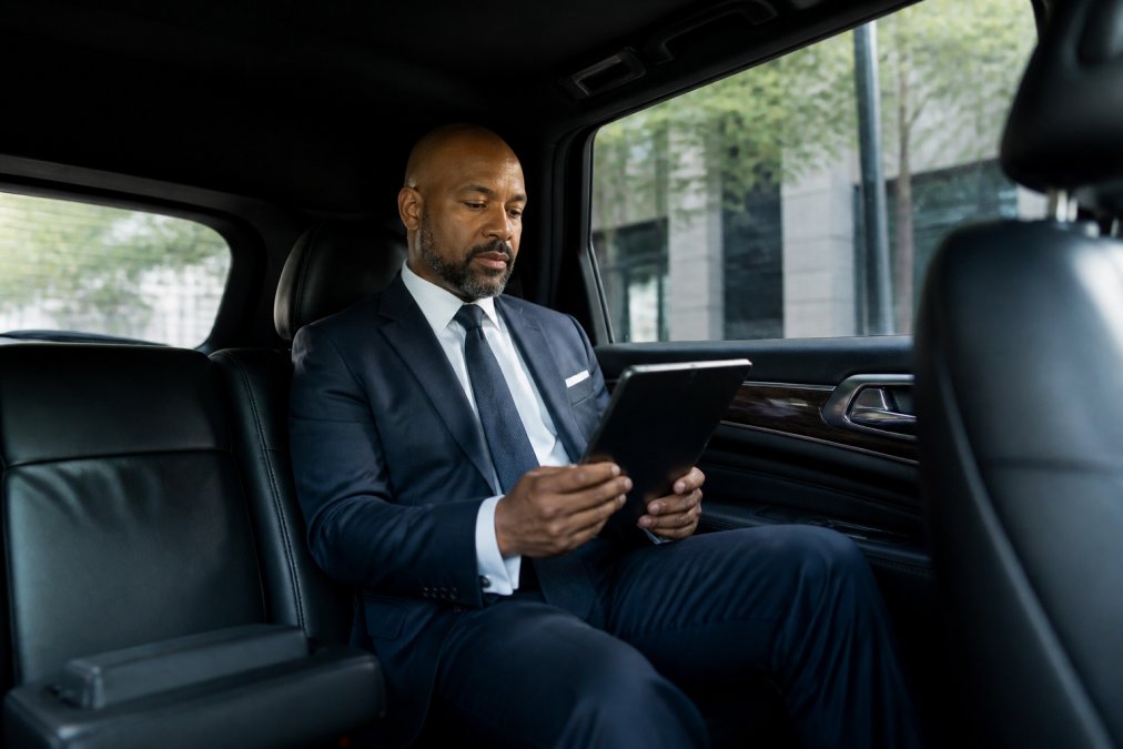 Professional business executive in a tailored suit sitting comfortably in the back of a luxury black SUV with a calm, confident expression while reviewing documents on a tablet during transit