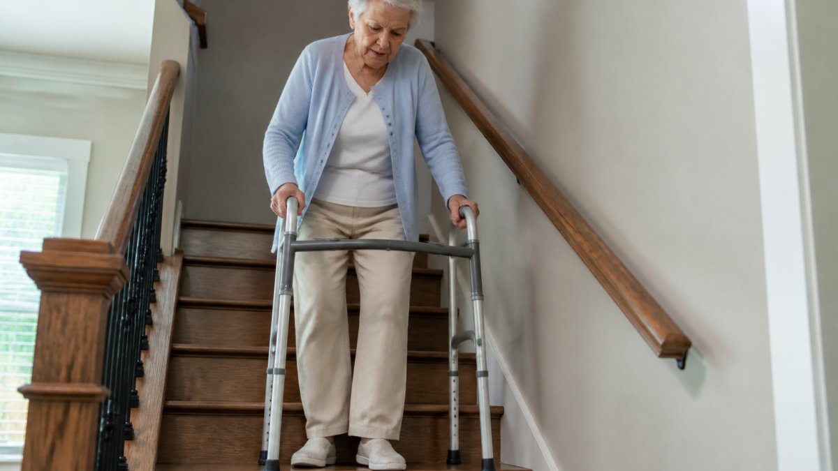 Older adult using a walker on a well-lit staircase with sturdy handrails, demonstrating safe stair use with mobility assistance