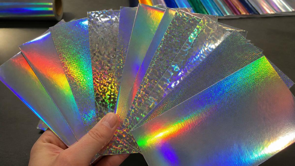 Close-up of holographic vinyl sample swatches displaying rainbow colour shifts at different angles with light reflecting across the surfaces to demonstrate spectrum changes and depth