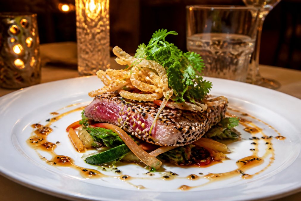A beautifully plated Asian fusion dish with vibrant colors on a white plate in a warm restaurant dining room with soft lighting and elegant table decor