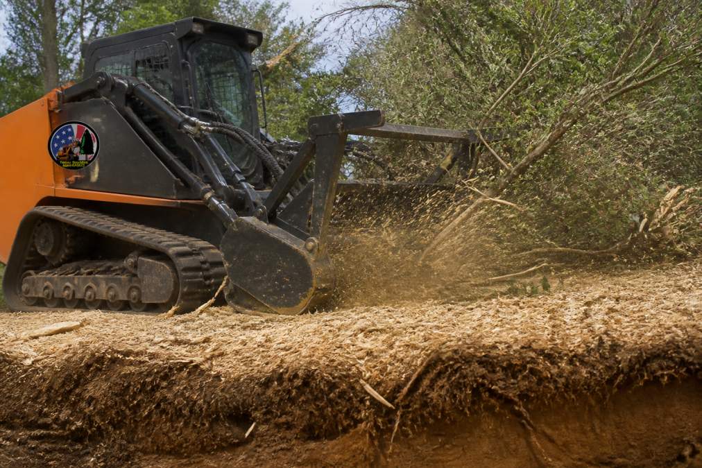 Professional forestry mulching equipment actively grinding dense brush and small trees into mulch on a cleared property, showing the layered mulch covering the ground and preserved topsoil underneath