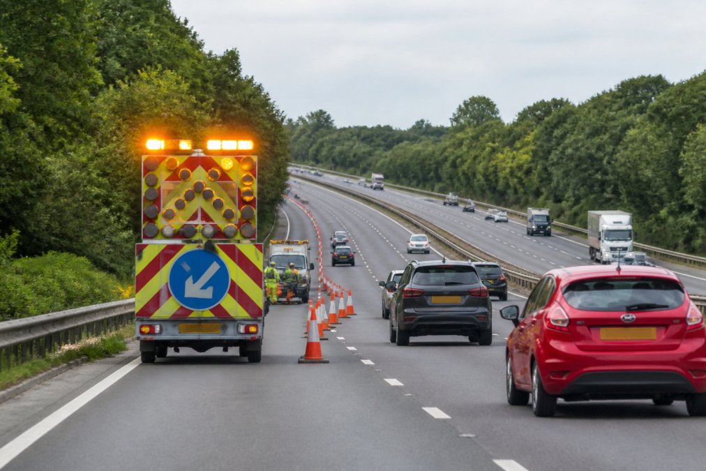 Amber vs Blue Hazard Lights: Which Works Best Professional roadwork operation with amber flashing beacon activated during daylight on a busy motorway, showing visibility from distance with multiple vehicles approaching, beacon mounted on construction vehicle